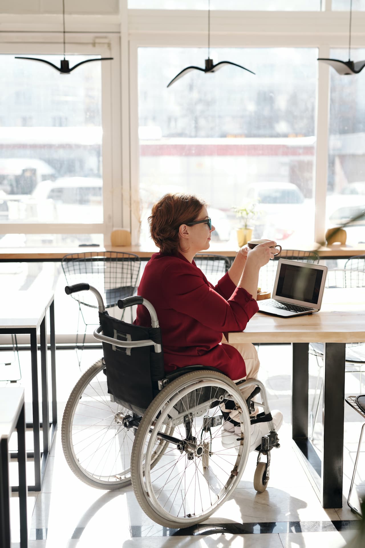 Woman in wheelchair working on laptop at café.