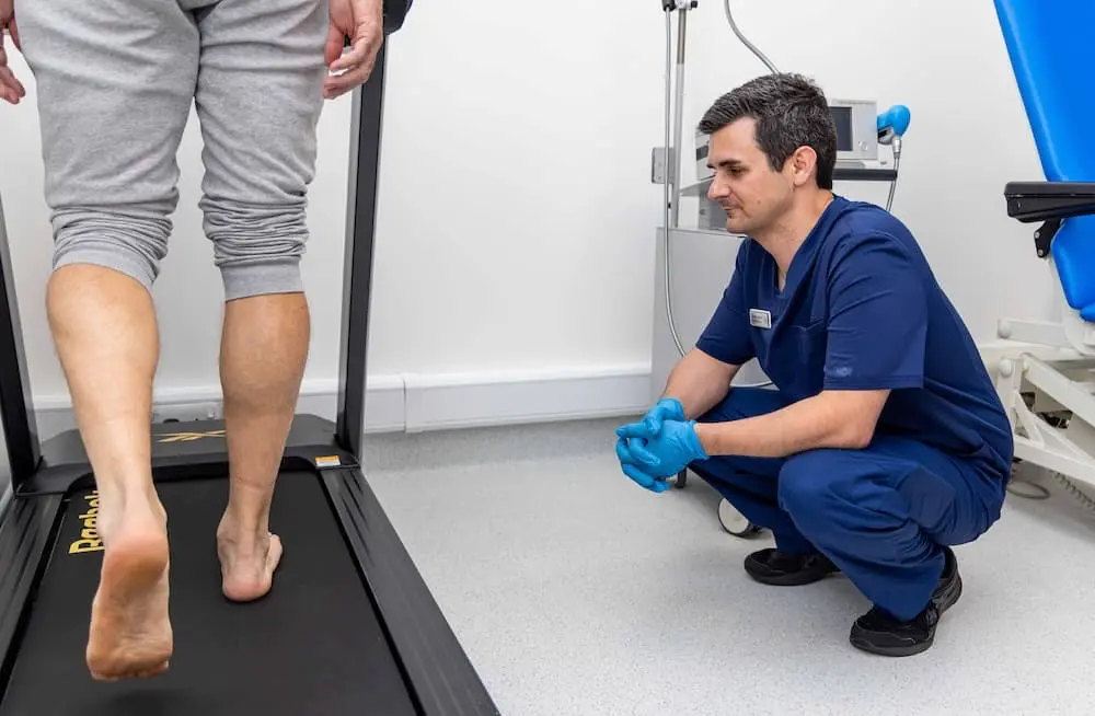 Physiotherapist observes patient walking on treadmill.